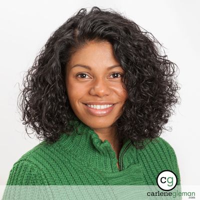 Professional business headshot of a woman with curly hair in a green sweater