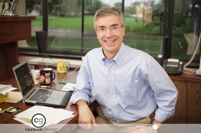 Executive portrait of a man at his desk with a laptop and campus view through the window